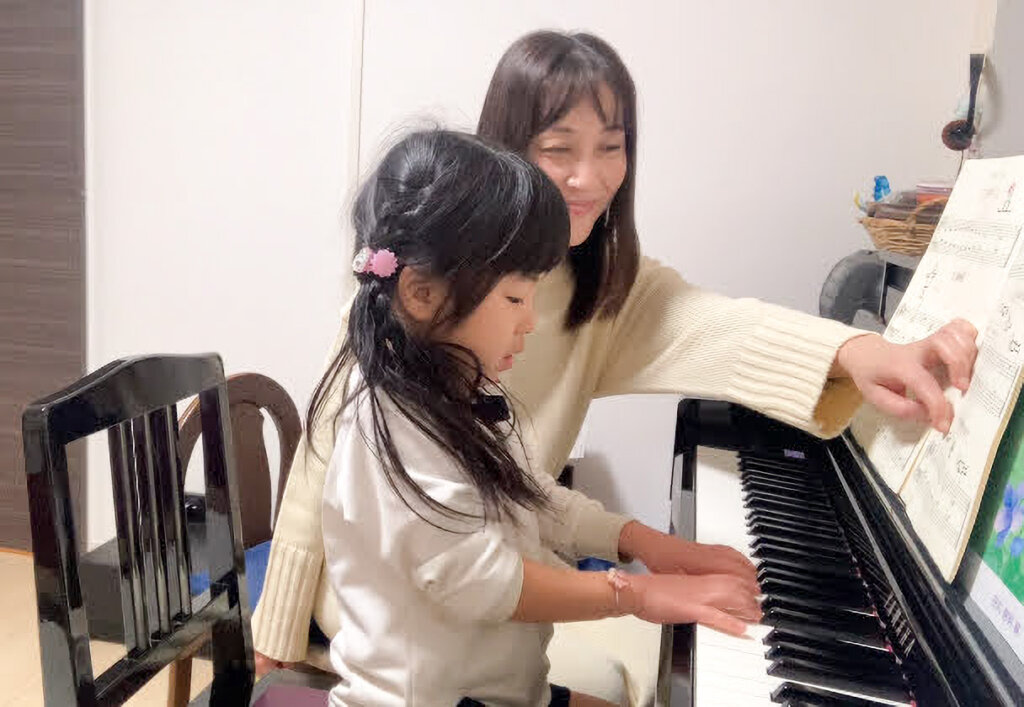 優しい表情でピアノを教えている講師と生徒